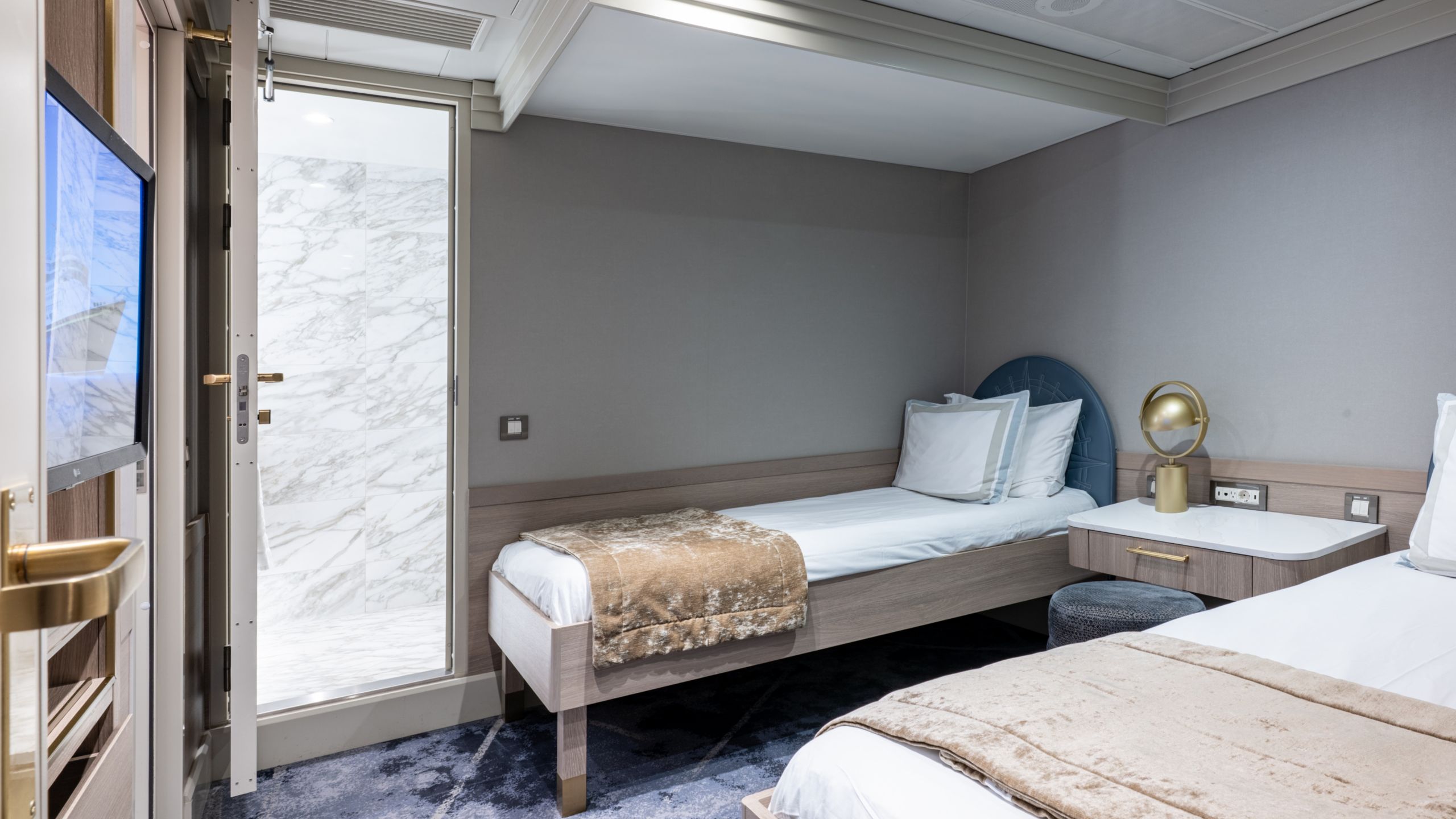 A bedroom with a TV, desk, stool, 2 beds and an adjacent bathroom in a Disney Wonder Concierge 2 Bedroom Suite with Verandah