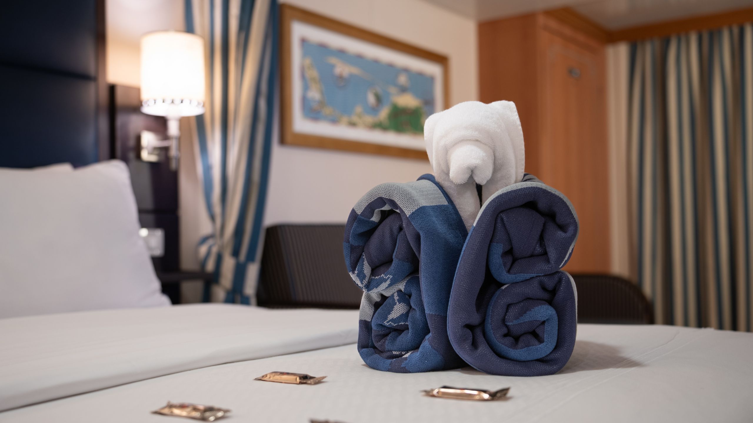 A Disney Wonder Deluxe Family Oceanview with Verandah Stateroom with chocolates and a decoratively folded towel on a bed