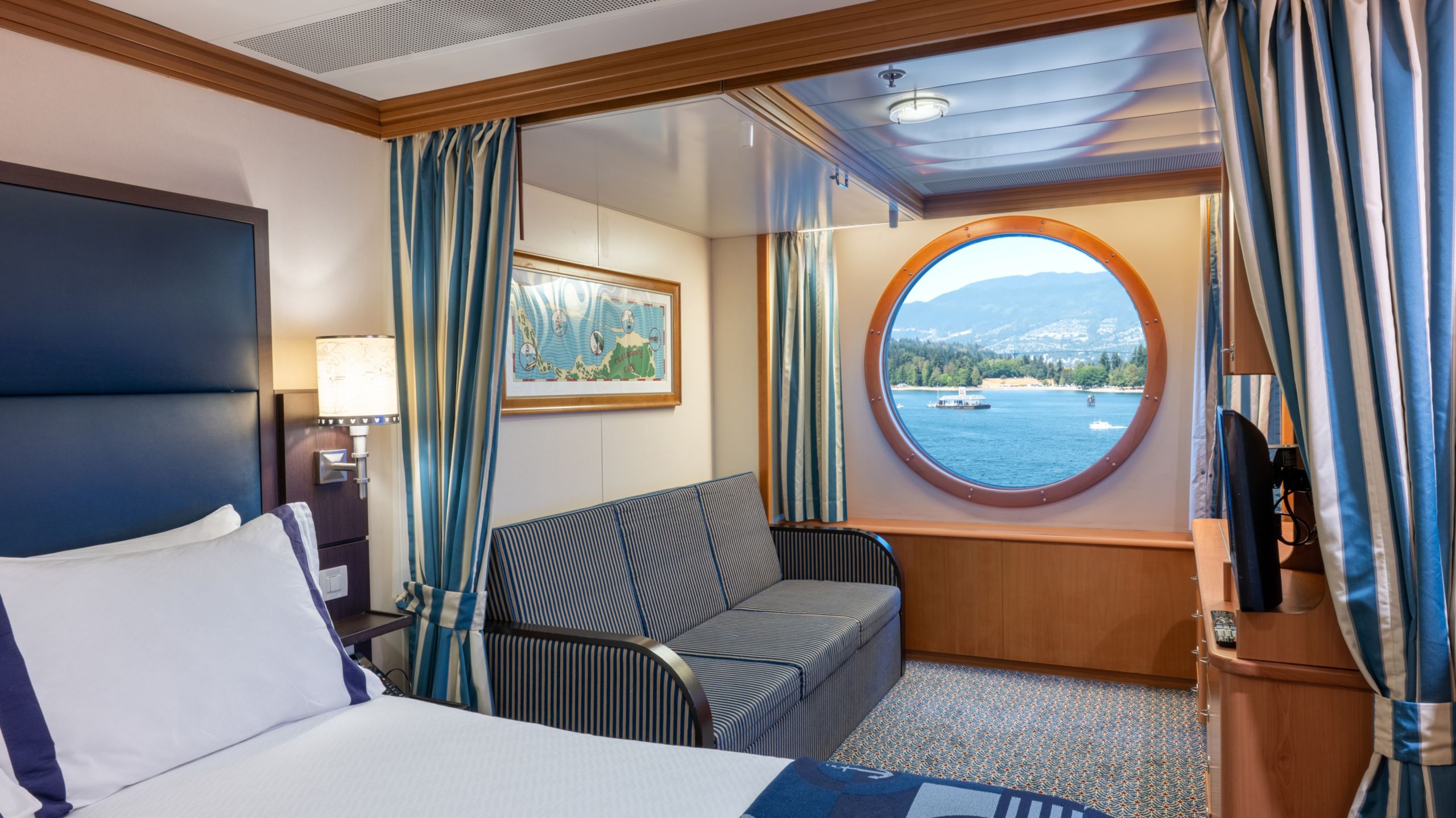 A Disney Wonder Deluxe Oceanview Stateroom with a bed, nightstand, desk, TV and 2 bunk beds