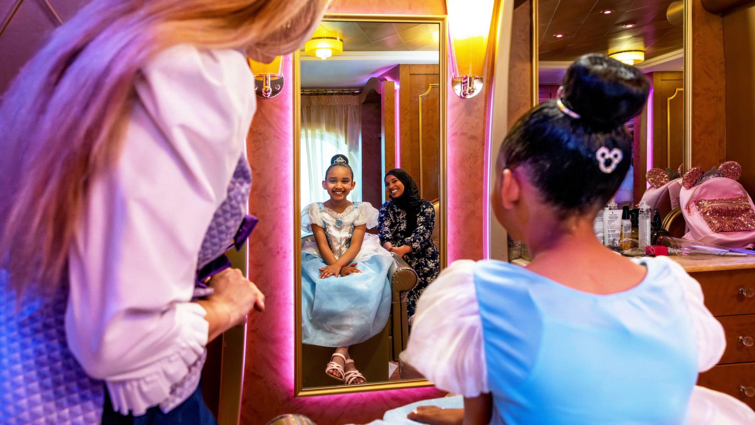 A young girl receiving a princess makeover from a Cast Member as her mother looks on