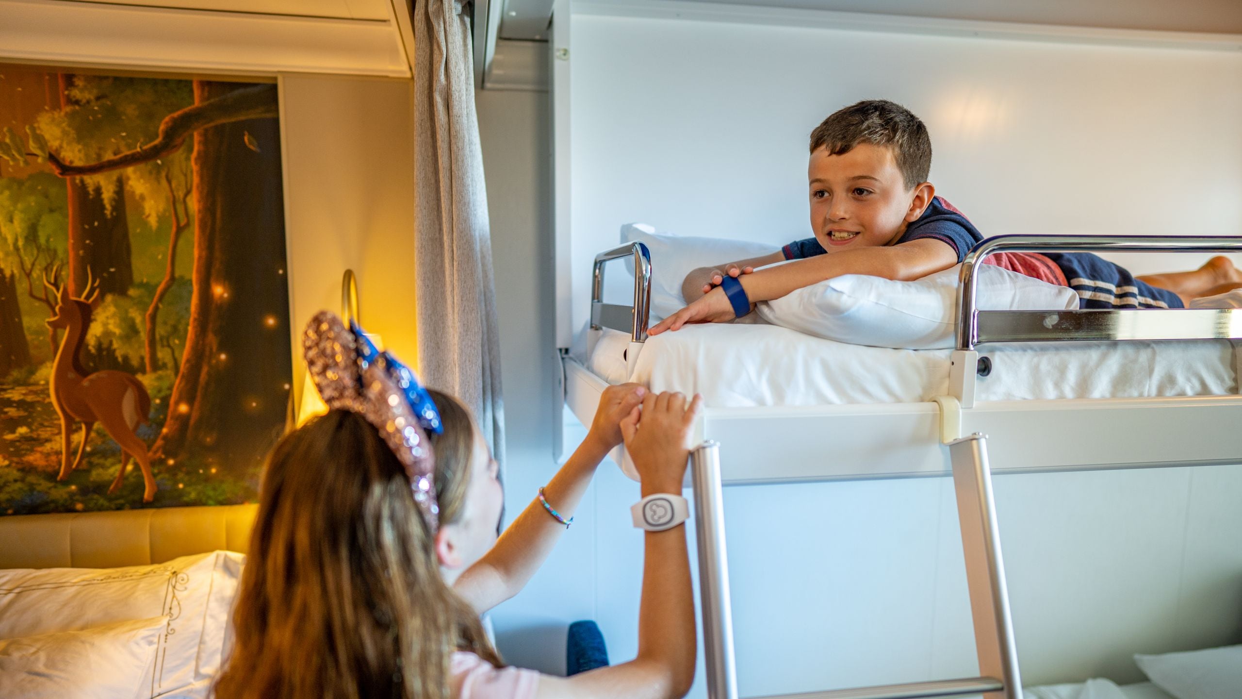 A sister talking to her brother as he lies in an upper bunk bed in a Disney Cruise Line stateroom with artwork inspired by The Princess and The Frog