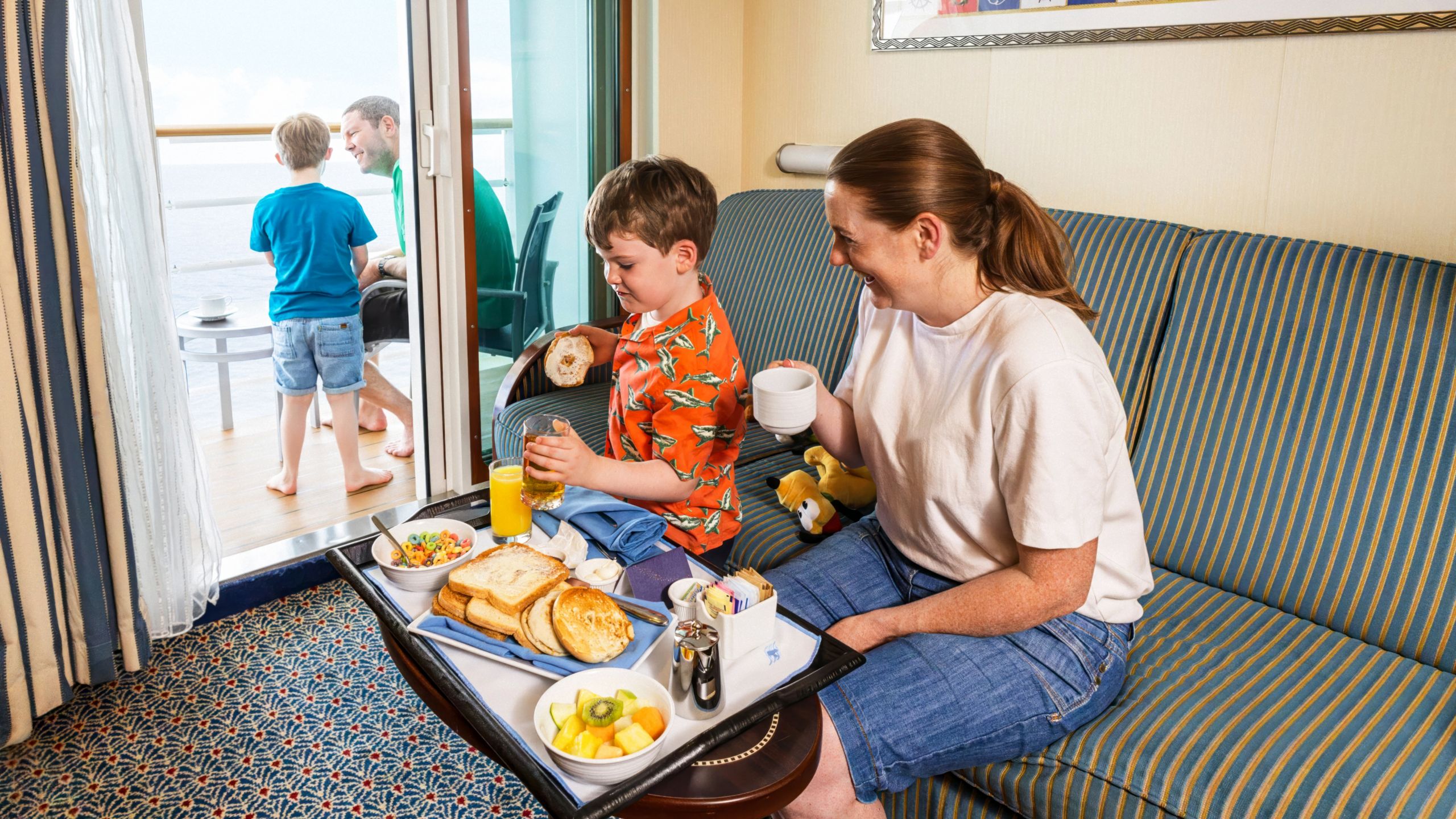 A family eating breakfast at a table and relaxing on a verandah in a Disney Cruise Line stateroom