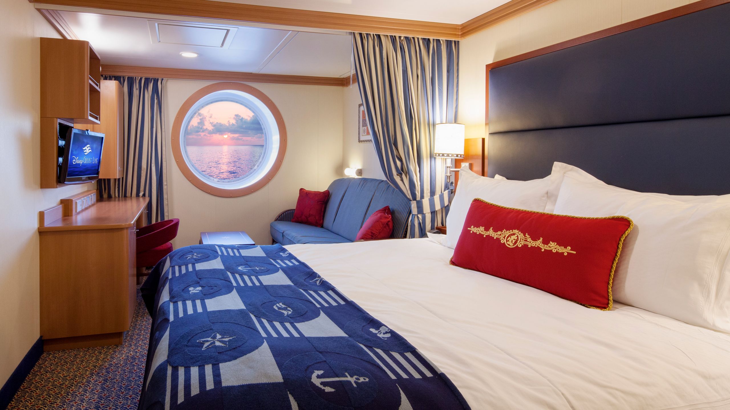 Un camarote con vista al mar del Disney Dream con cama, escritorio, silla, sofá, TV, mesa, mesa de noche y un balcón con vista al mar