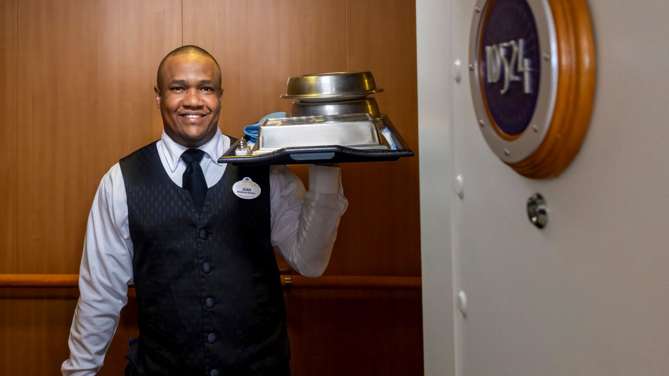 A Disney Cruise Line Cast Member carrying a tray of dishes