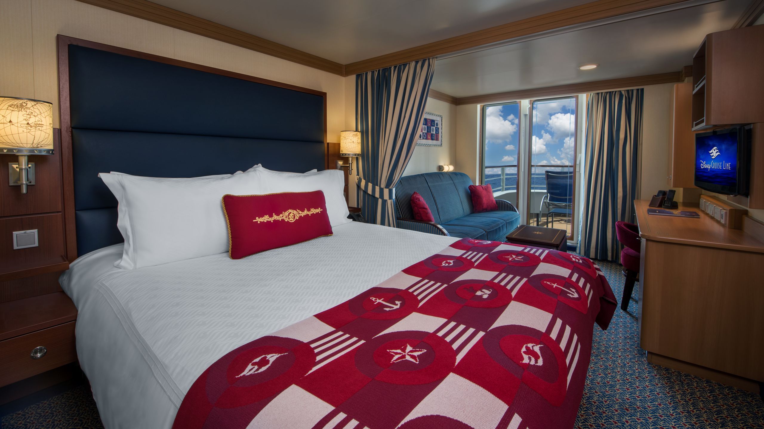A Disney Dream stateroom with a bed, sofa, table, desk, TV, 2 nightstands and a verandah facing the ocean