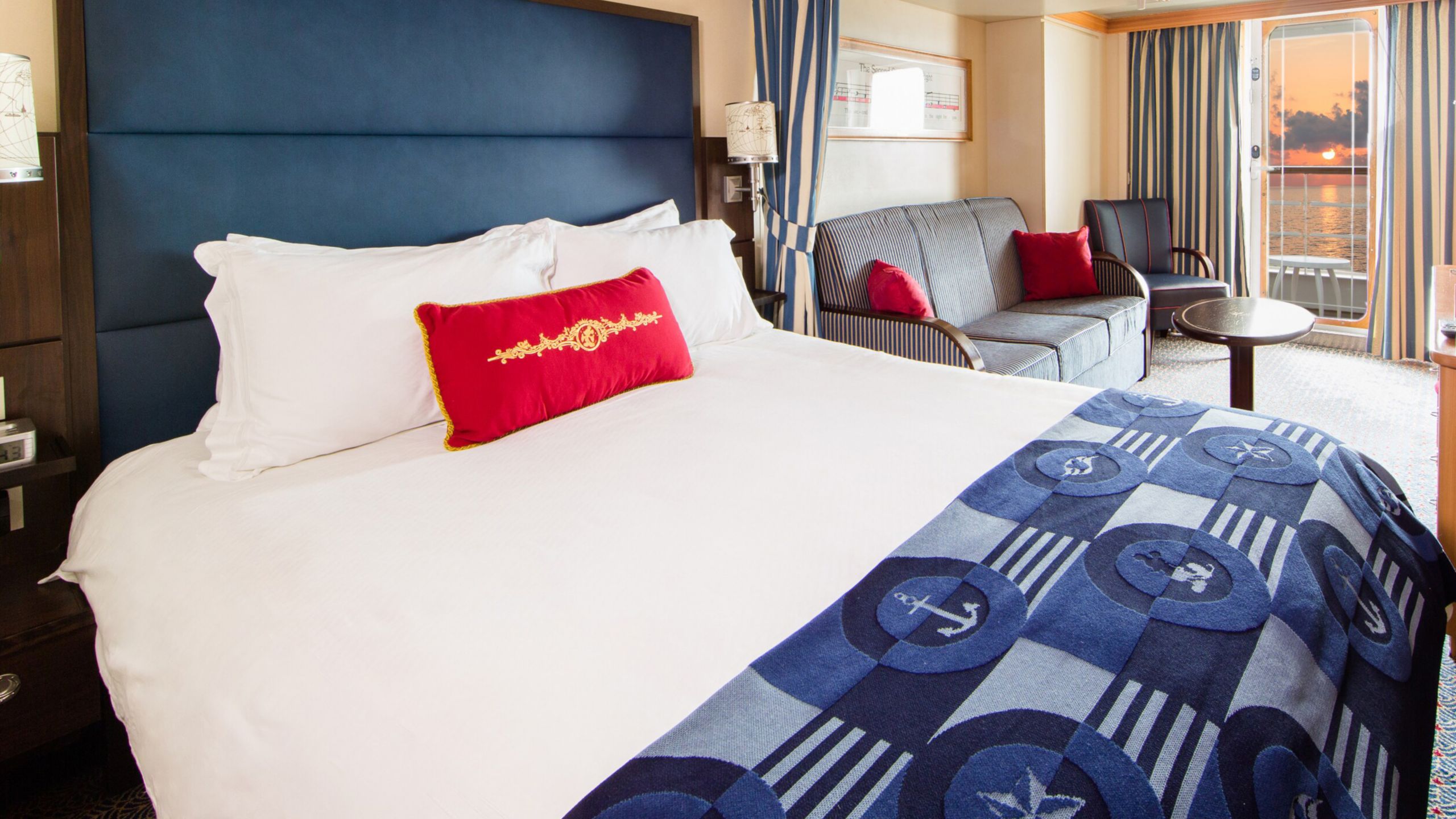 A Disney Cruise Line stateroom with a bed, sofa, table, desk, chair, 2 nightstands and a verandah facing the ocean