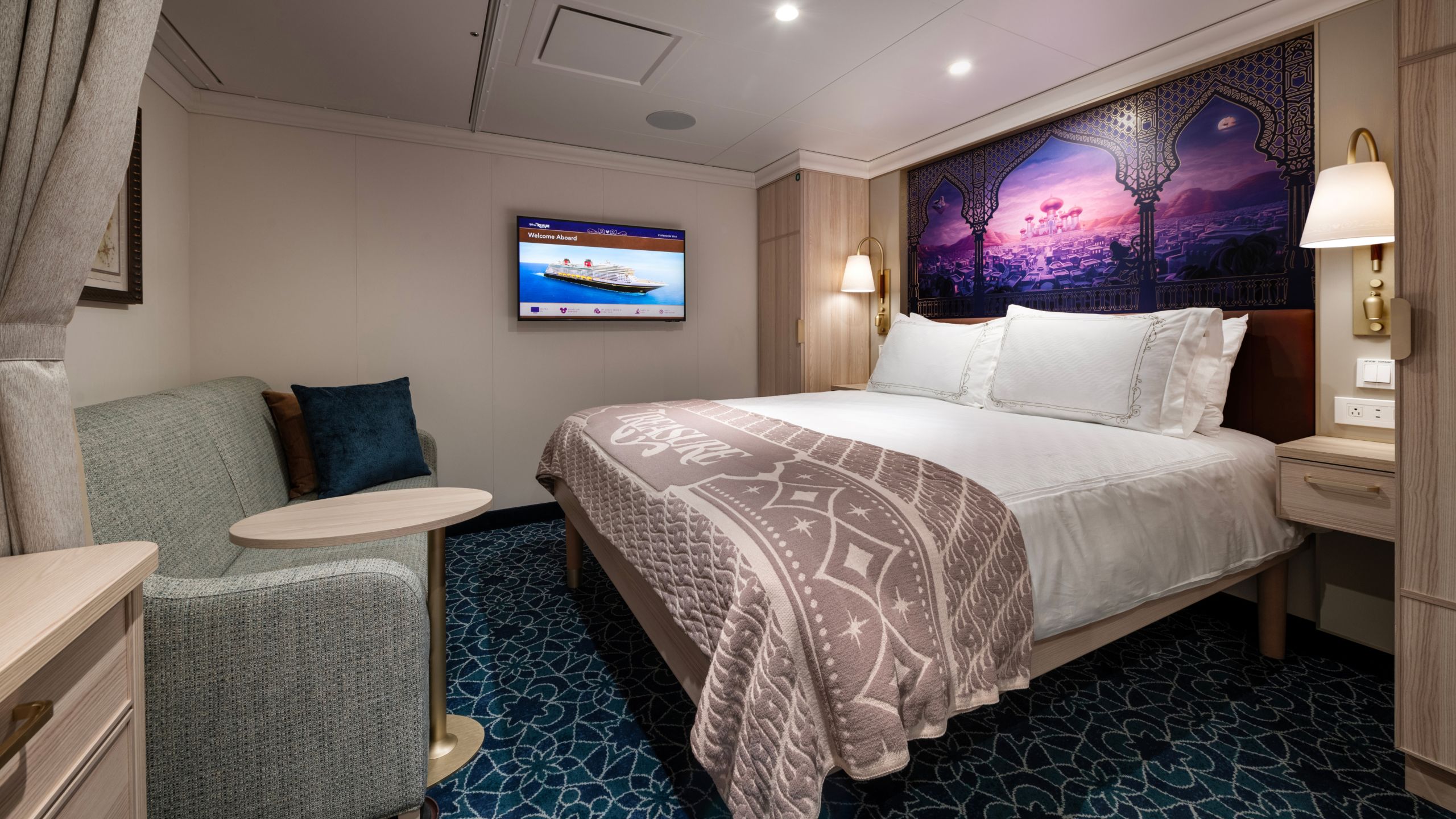 Un camarote del Disney Treasure con cama, sofá, mesa, televisor y dos mesas de noche