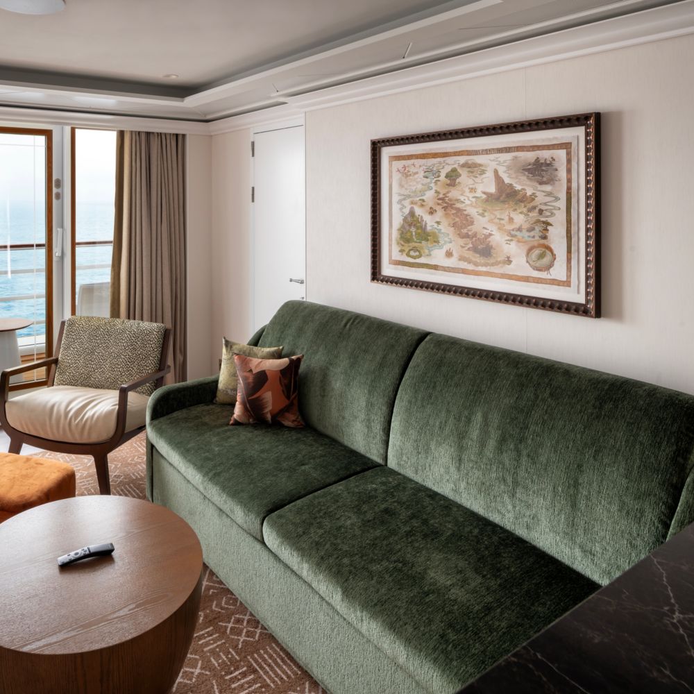 Un camarote del Disney Treasure con sofá, televisor, mesa de centro, silla, balcón y arte inspirado en el Rey León