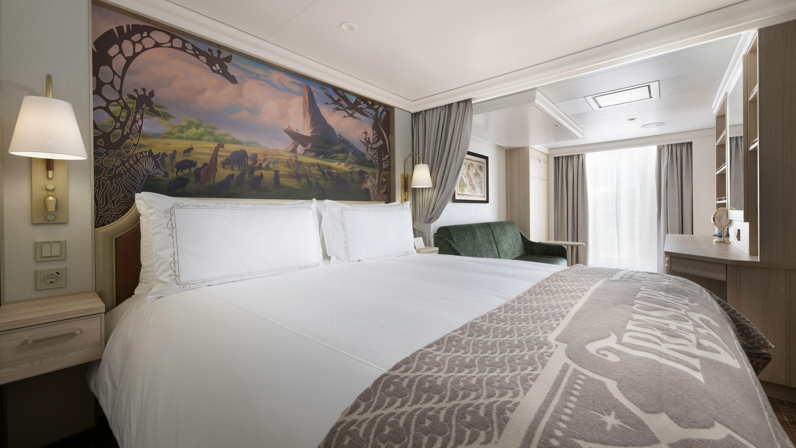 Un camarote del Disney Treasure con una cama, sofá, escritorio, dos mesas de noche y obras de arte inspiradas en el Rey León