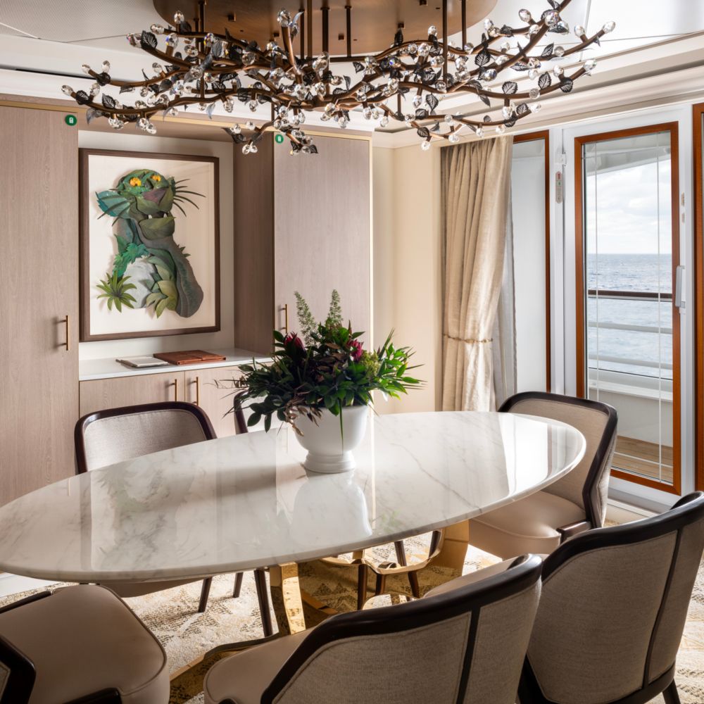 Un camarote del Disney Cruise Line con una mesa de comedor, lámpara de techo, mesa de comedor, seis sillas, gabinetes, obras de arte inspiradas en el Libro de la Selva y un balcón