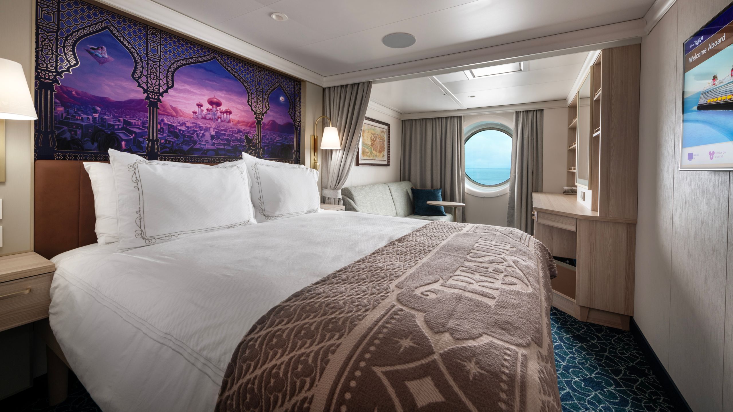 An artist rendering of a Disney Treasure Deluxe Oceanview Stateroom with a bed, a sofa, a porthole with an ocean view and a vanity