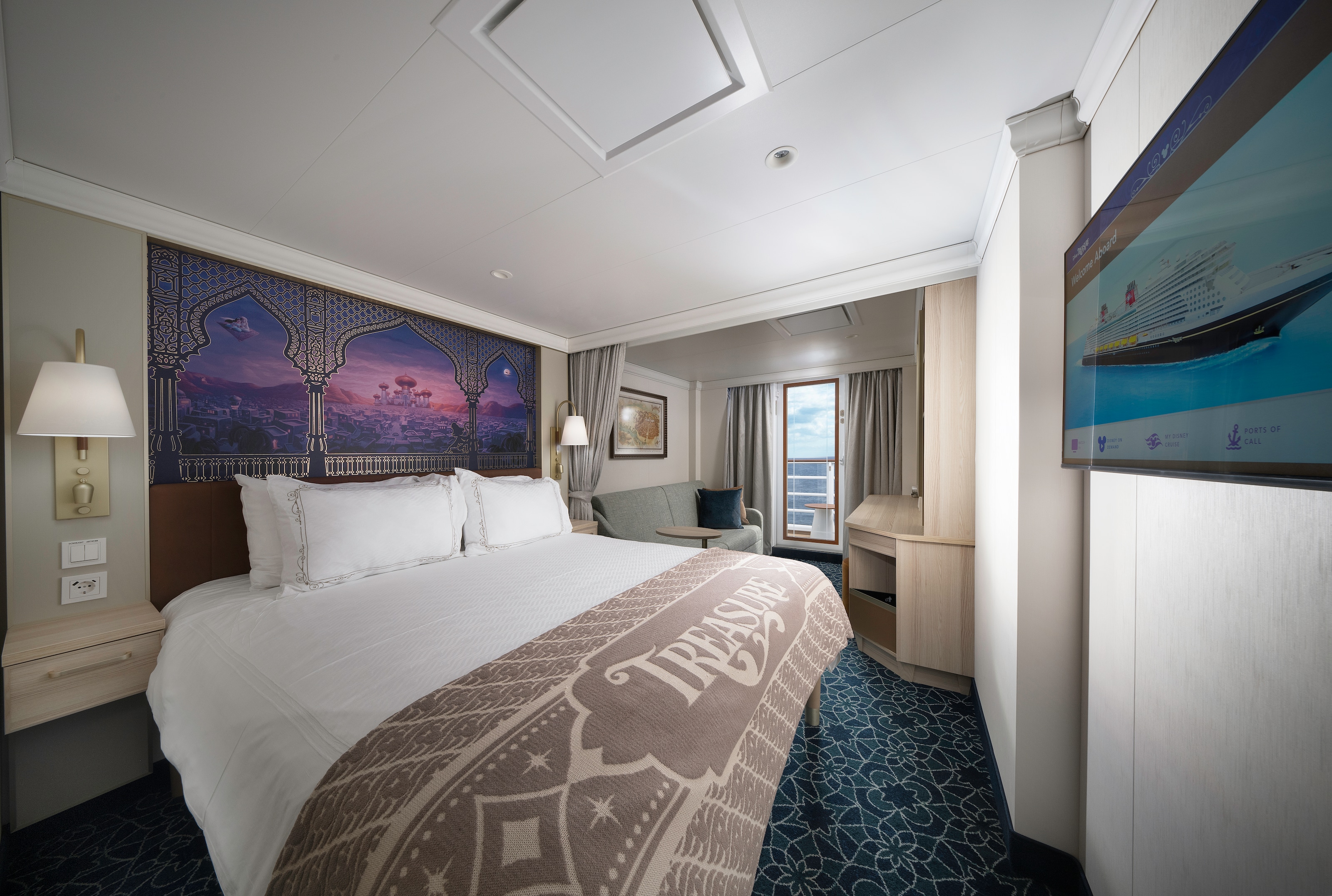 A Disney Cruise Line Verandah Stateroom with a bed, table, artwork inspired by Aladdin, sofa, desk, 2 nightstands and a verandah facing the ocean