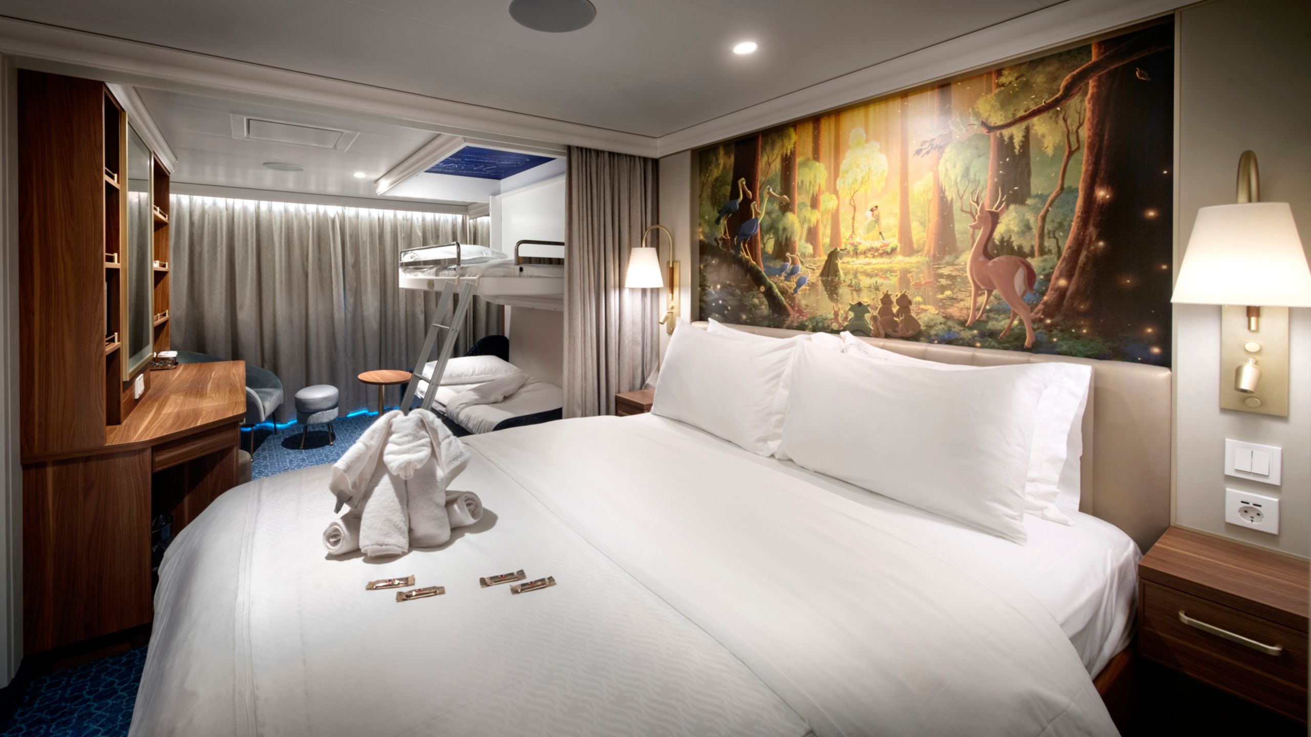 Un Camarote Familiar de Lujo con Vista al Mar del Disney Wish, con cama, sofá, mesa, silla, escritorio, obras de arte inspiradas en La Princesa y el Sapo, dos mesas de noche y una ventana con vista al mar