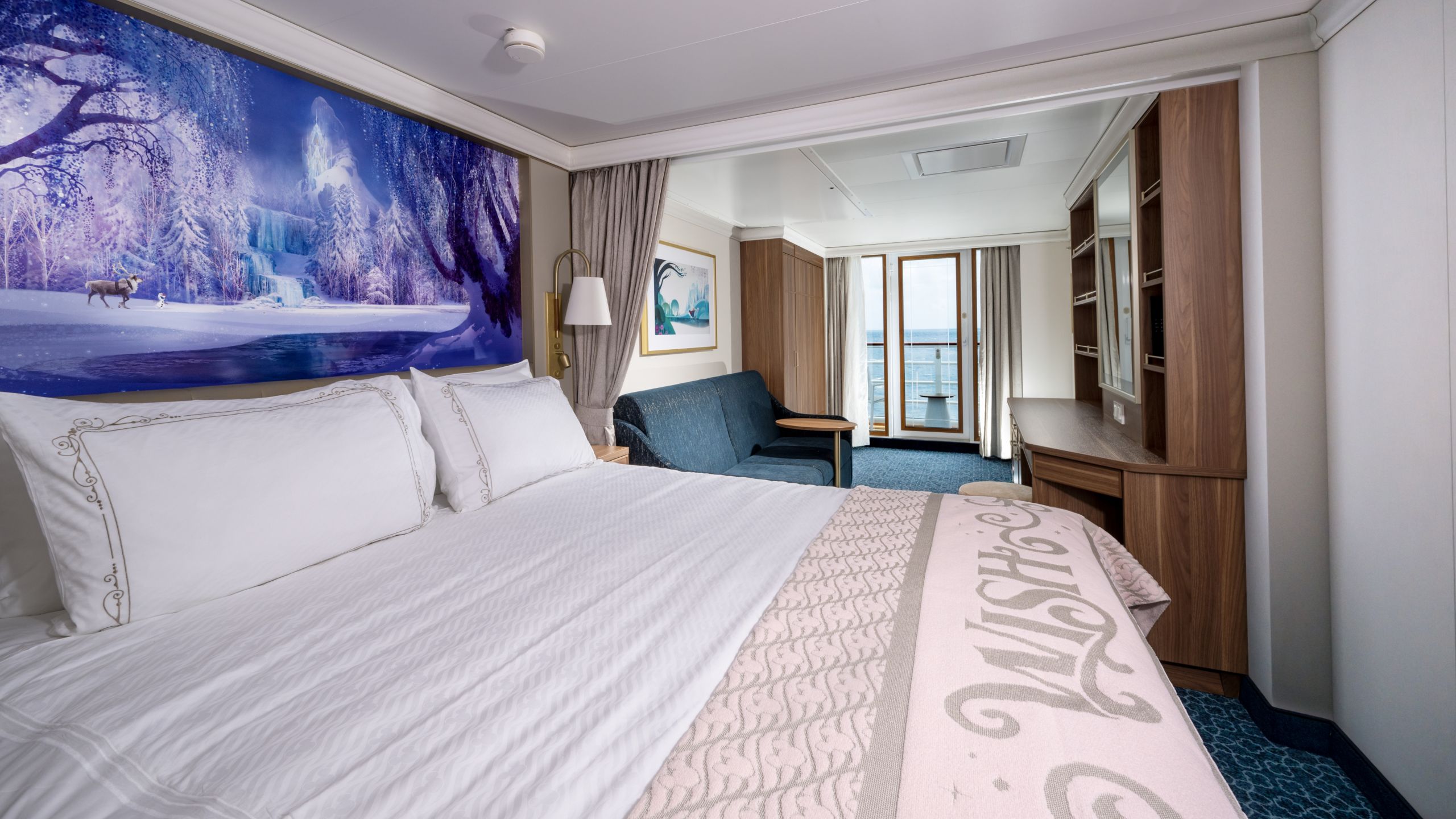 A Disney Wish stateroom featuring a bed, sofa, desk, artwork inspired by Frozen and a verandah
