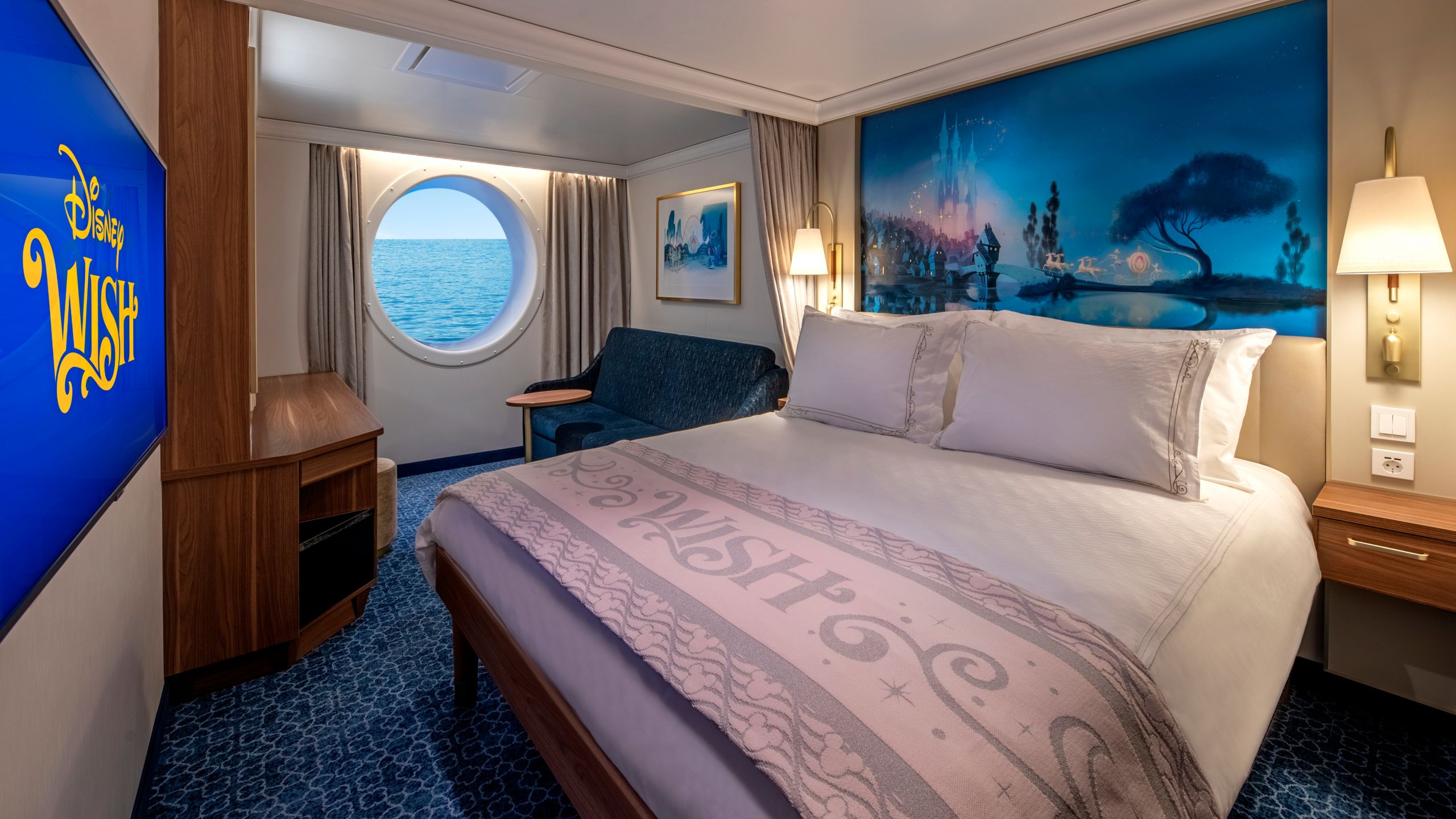 Un Camarote de Lujo con Vista al Mar del Disney Wish, con cama, sofá, mesa, escritorio, espejo, televisión, obras de arte inspiradas en Cenicienta y una ventana con vista al mar