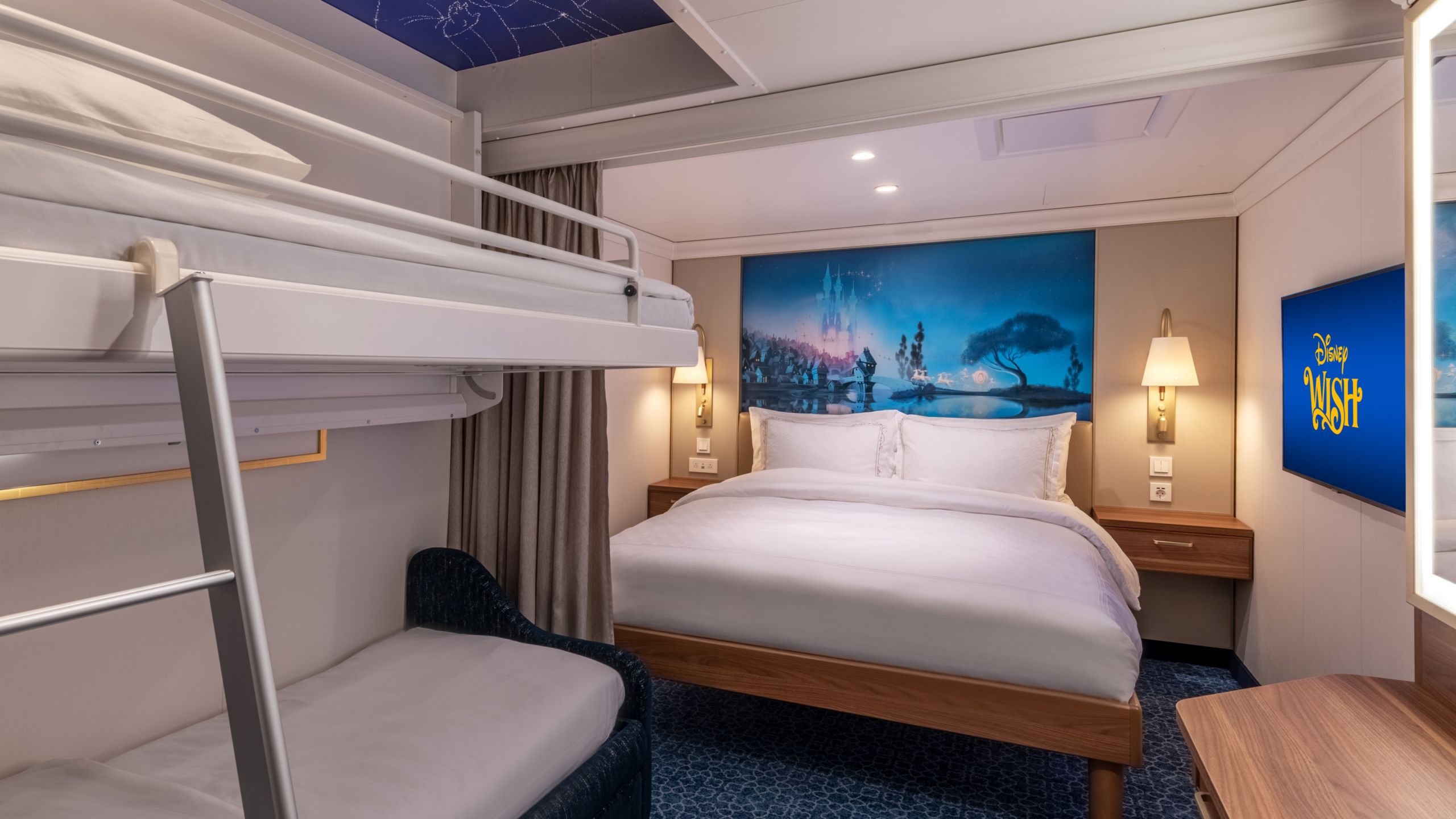 A Disney Wish Inside Stateroom with a bed, sofa, desk, mirror, TV, 2 nightstands and artwork inspired by Cinderella