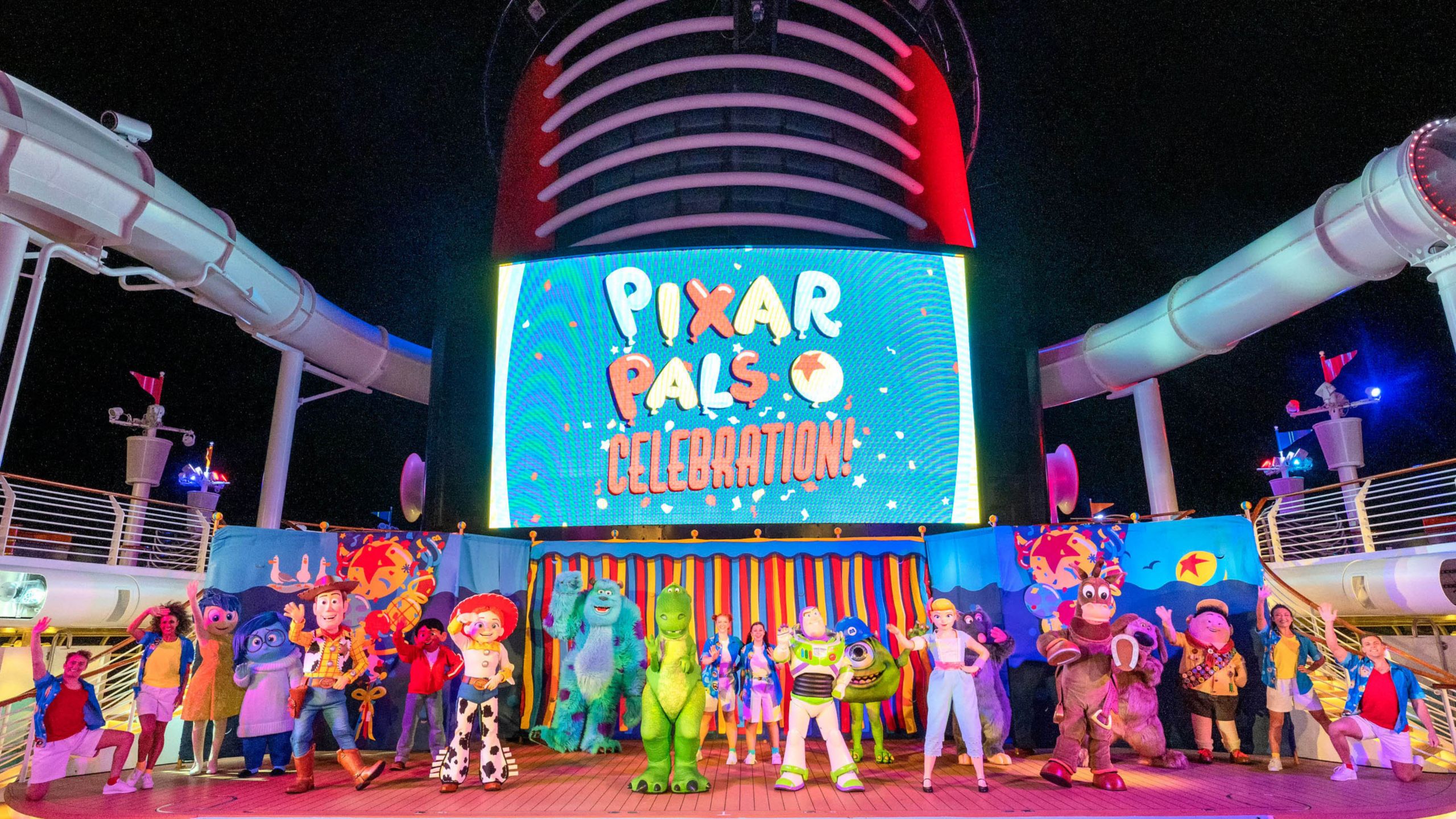 Pixar Characters waving on the deck of a Disney cruise ship with a screen that reads ‘Pixar Pals Celebration’