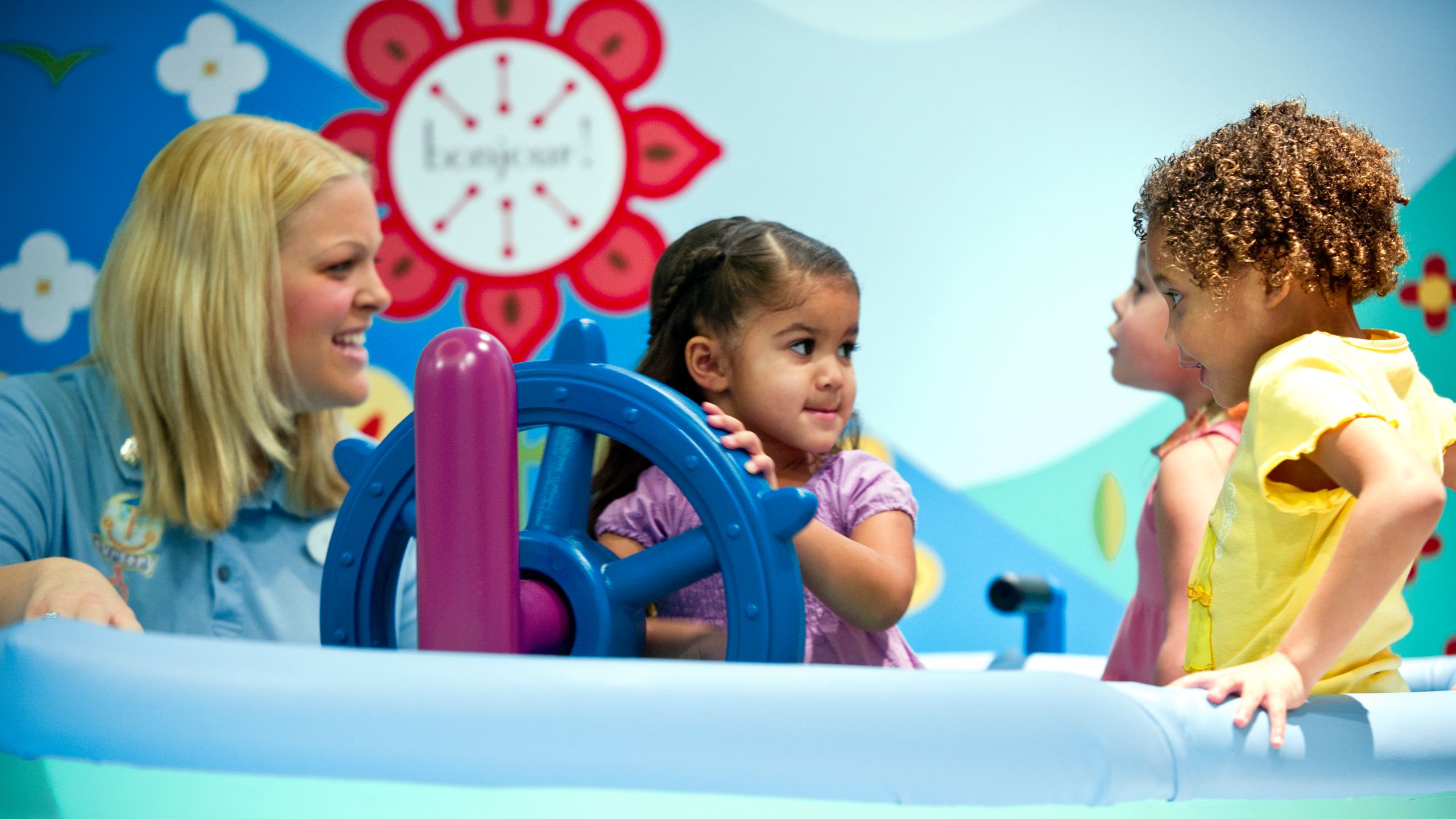 A young girl steers the wheel on a play ship along with a Cast Member and 2 young girls 