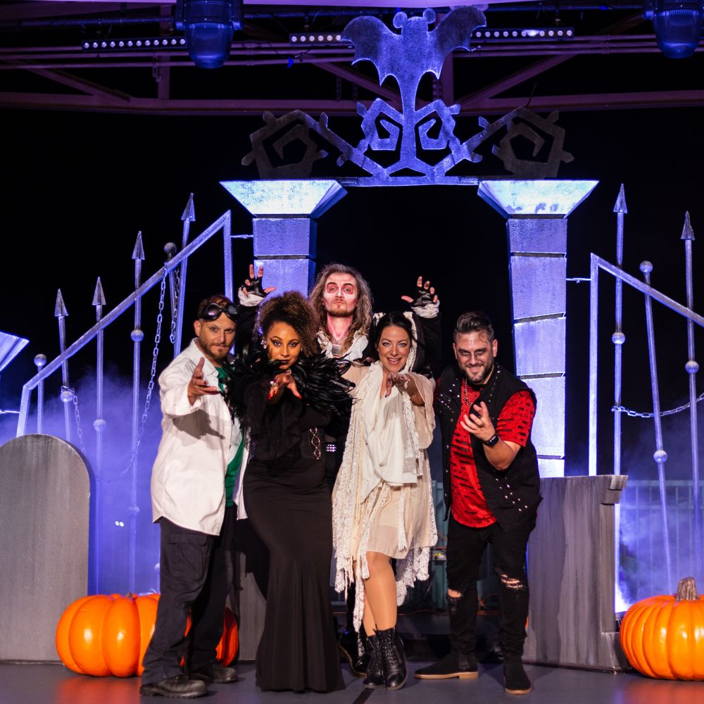 Squad Ghouls, an acapella group posing onstage for a photo surrounded by tombstones and pumpkins at Mickey’s Not So Scary Halloween Party
