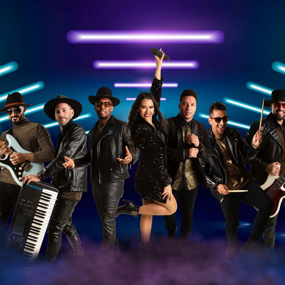 The 7 member band, Stella Beat, posing for a photo with various musical instruments including a guitar, a bass guitar, drum sticks and a keyboard