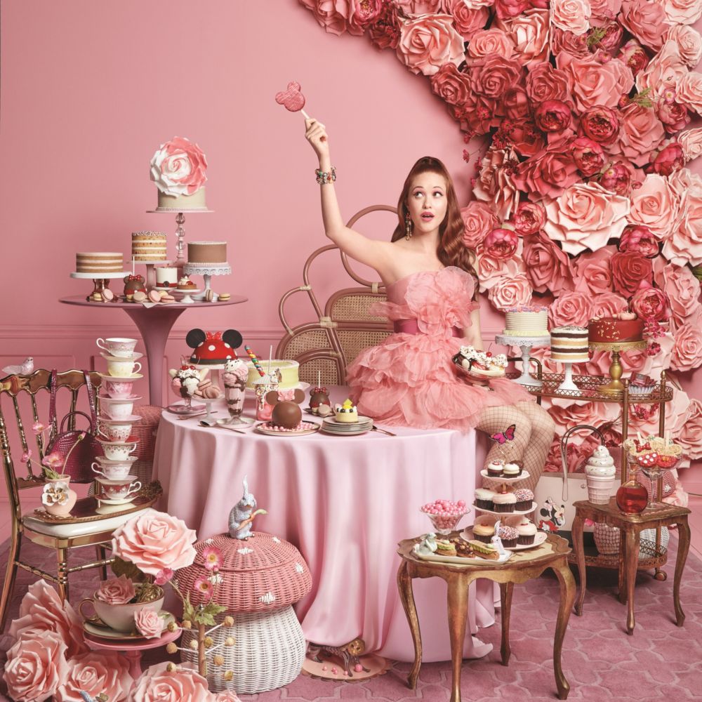  A woman in a frilly dress at a table piled high with Mickey Mouse shaped treats, teacups and flowers
