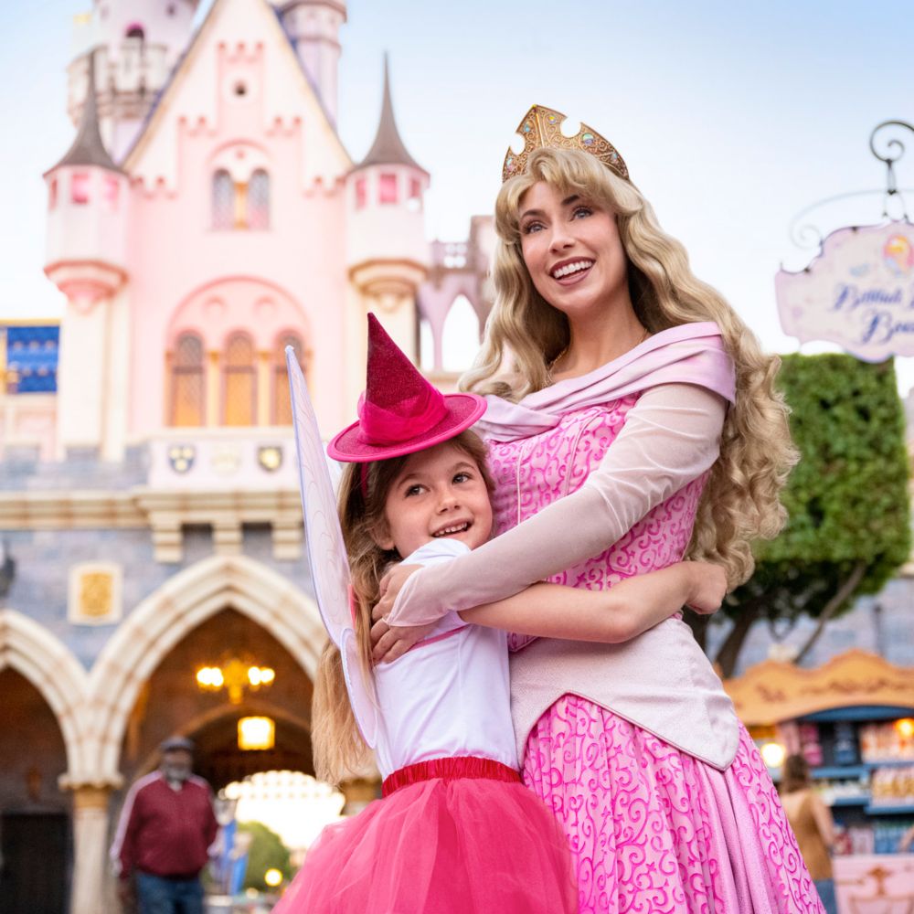 A girl hugging Princess Aurora in front of Sleeping Beauty Castle