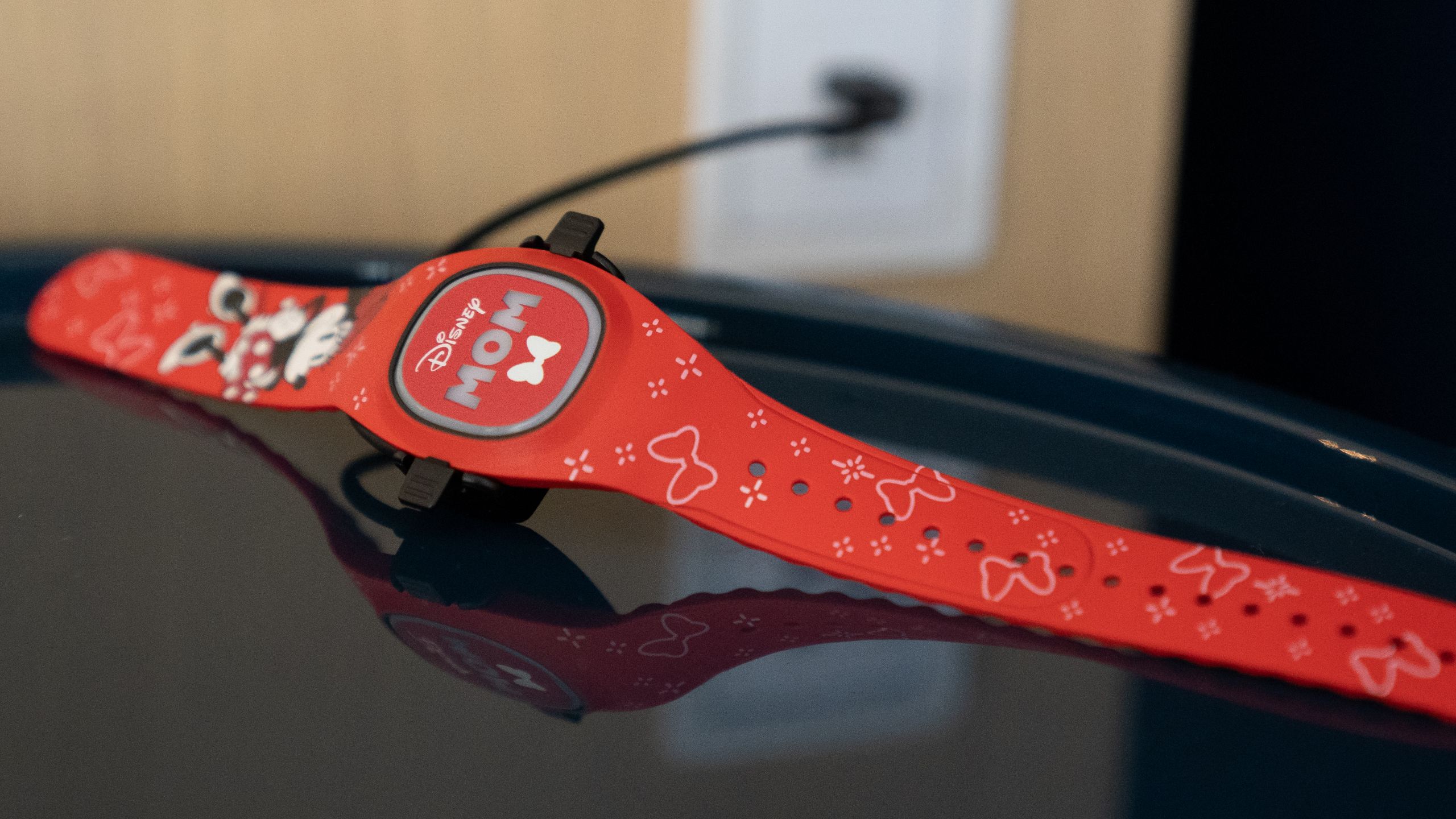 A Disney Band Plus with the Disney logo and the word Mom on its face plugged into a wall