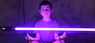 A child meditating with a purple lightsaber