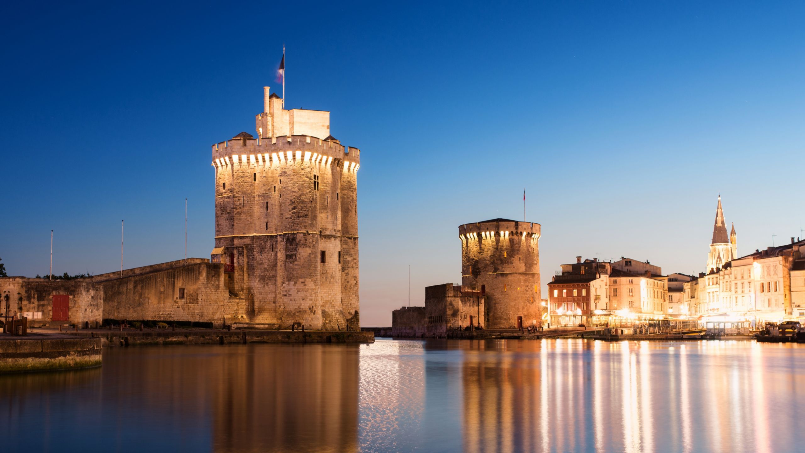 The medieval stone towers of La Rochelle, Tour Saint Nicolas and Tour de la Chaîne, standing guard over the water of the Old Port illuminated at dusk