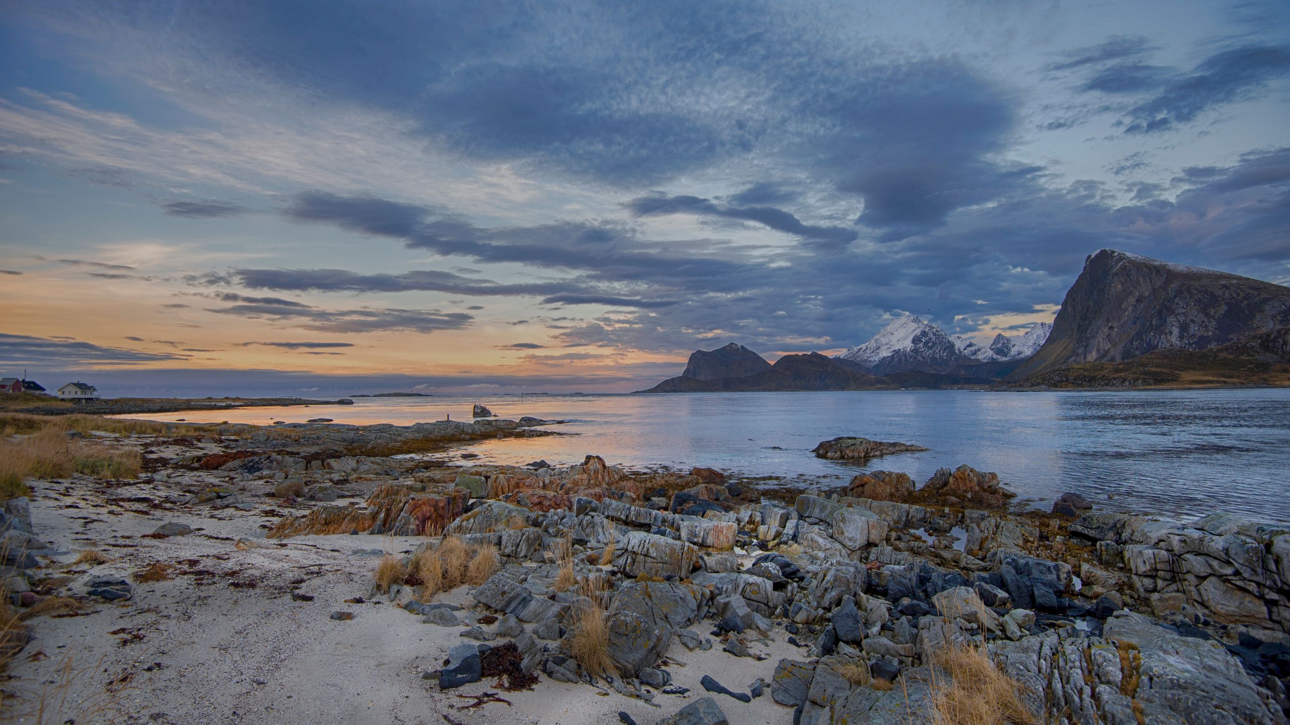 A rocky beach on a calm fjord with mountains under a cloudy sunset