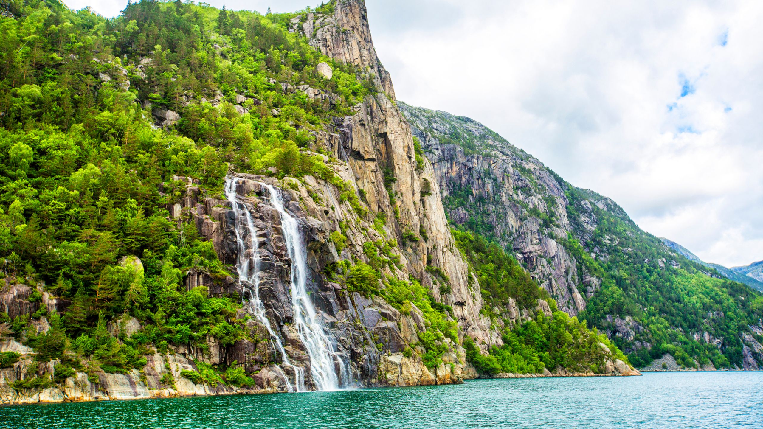 A waterfall cascading down a steep forested cliff into a fjord