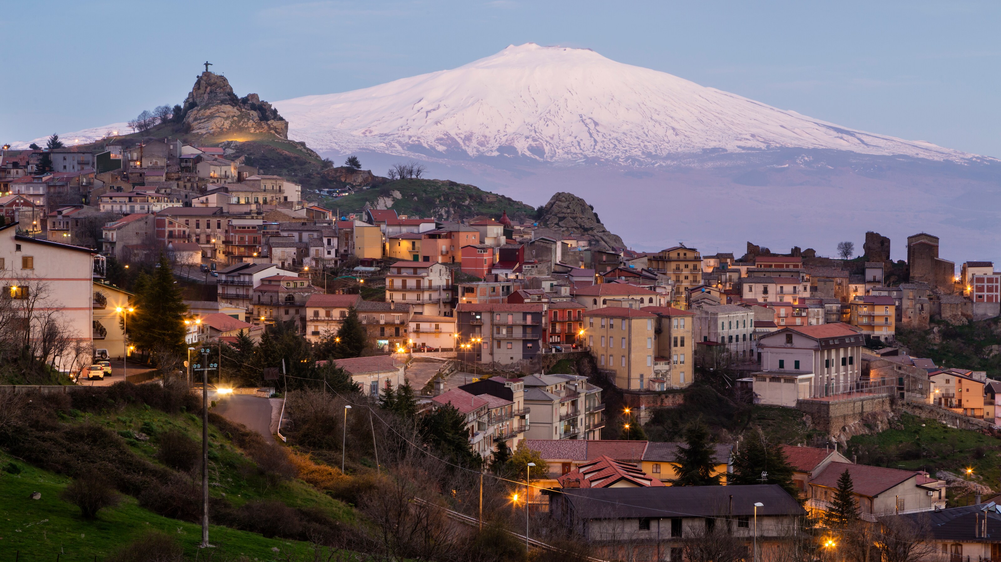 A village built into a mountainside next to a snowcapped volcano