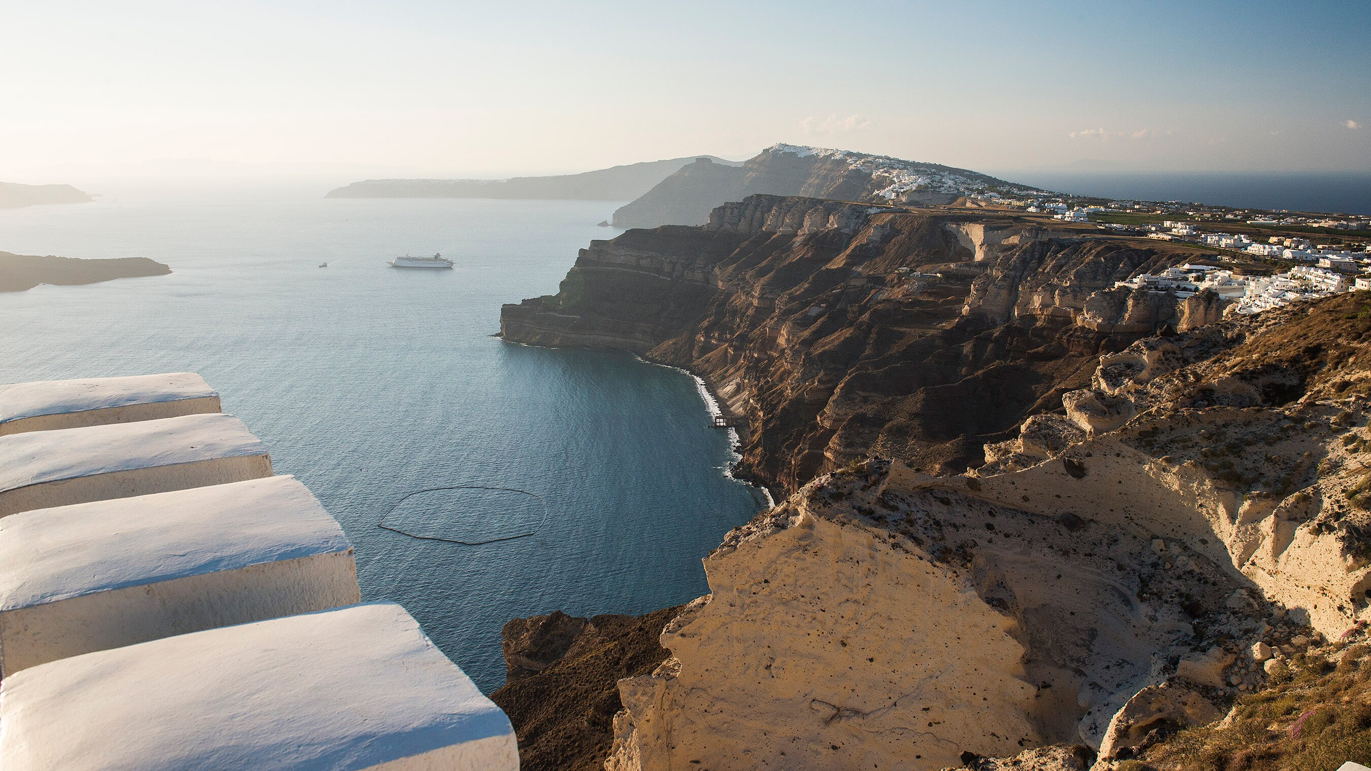 A Disney cruise ship surrounded by dramatic coastal cliffs