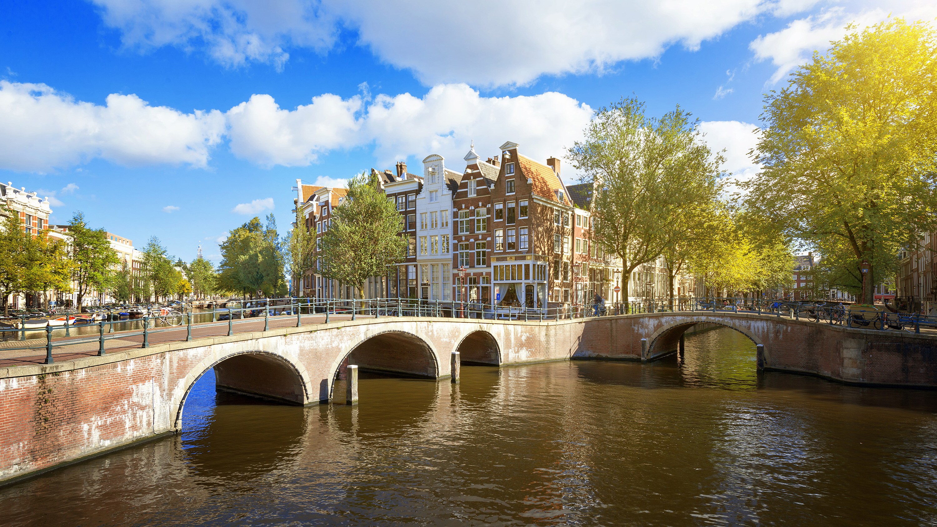 A canal in Amsterdam with arched brick bridges, historic canal houses and leafy trees